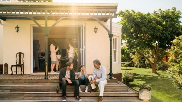 Family engaged in a conversation; some members are inside the home while others are sitting on the stairs outside.