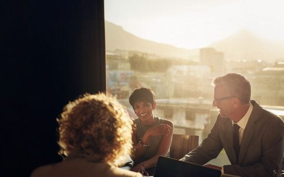 A candid photograph of three people in a professional yet relaxed meeting setting