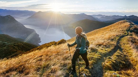 Woman on the top of the mountain climbing and watching sun above horizon