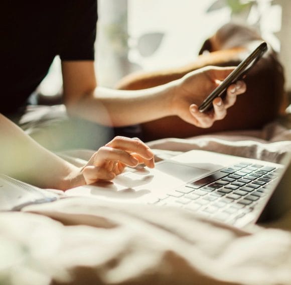 A person holds a mobile phone with one hand while using a computer with the other.