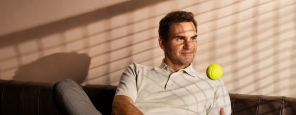 Roger Federer sitting on a couch and playing with a tennis ball.