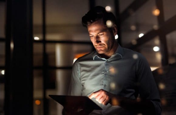 adult man looking at his iPad in a nighttime setting while tapping on the screen.