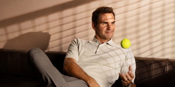 Roger Federer sitting on a couch and playing with a tennis ball.
