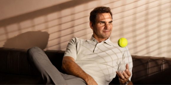 Roger Federer sitting on a couch and playing with a tennis ball.