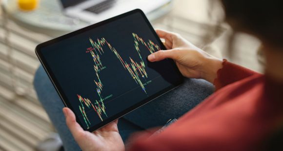 Pessoa segurando um tablet exibindo gráficos financeiros e oscilações do mercado de ações na tela