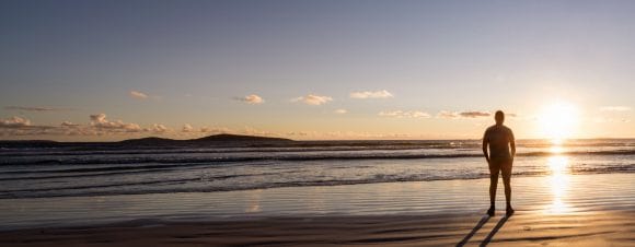  Man standing on beach looking at the sunset