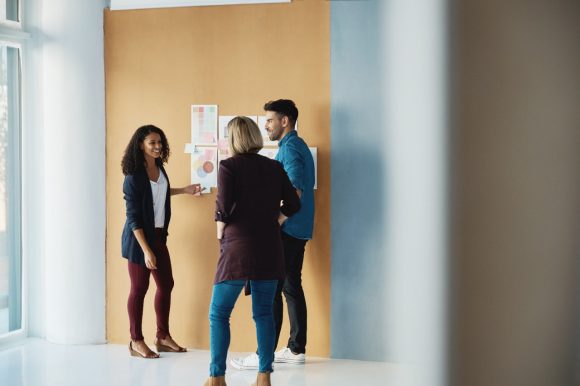 Un groupe de 3 personnes discutent d’un plan financier affiché sur un mur.