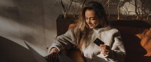 Rothaarige Frau im ockerfarbenen Pullover, die ein Smartphone anlächelt
