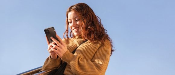 Rothaarige Frau im ockerfarbenen Pullover, die ein Smartphone anlächelt