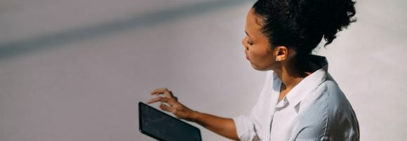 Schwarze Frau mit lockigem Haar zu einem Dutt gebunden, sitzt und hält ein Tablet