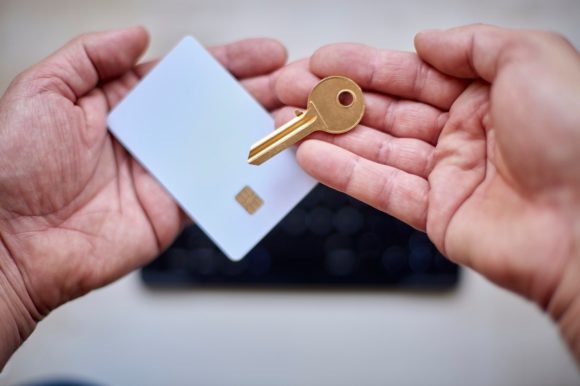 Hände einer erwachsenen Person halten Bezahlkarte und Schlüssel.