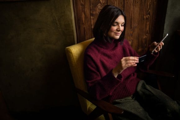 Eine junge Frau kauft mit ihrem Handy und ihrer Kreditkarte online ein.