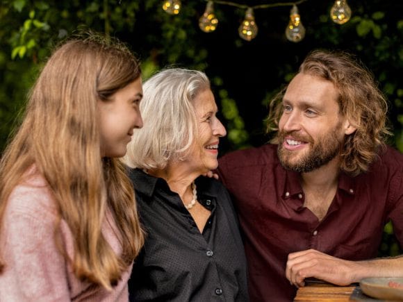 Drei Generationen sitzen in einem Garten zusammen.