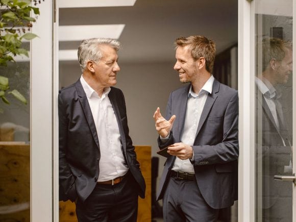 Zwei Männer in Anzügen unterhalten sich an einer Glastür.
