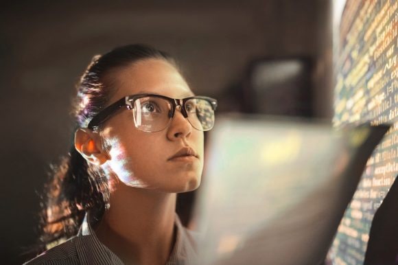 Frau analysiert Computercode an einer Wand – Cyber Security Konzept.