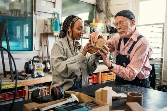 Senior gentleman working with young woman at workbench.