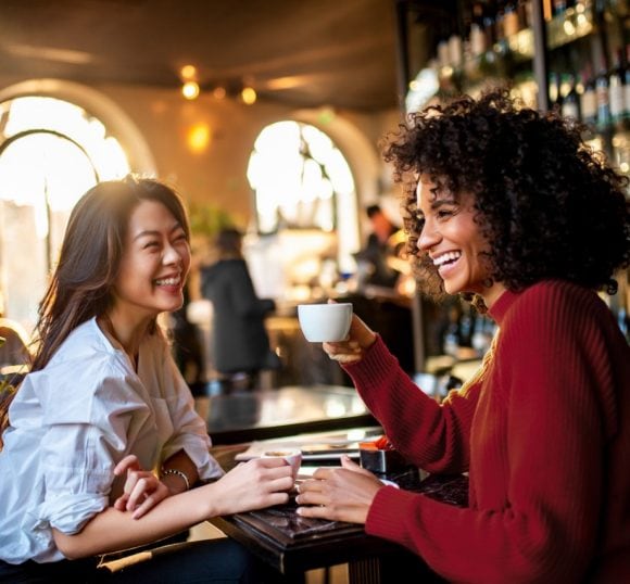 Zwei Frauen unterhalten sich lachend in einem Café.