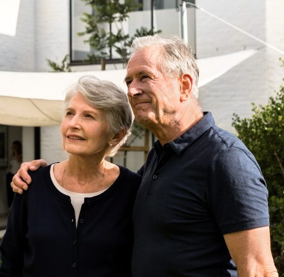 Älteres Paar steht im Garten vor seinem Haus.