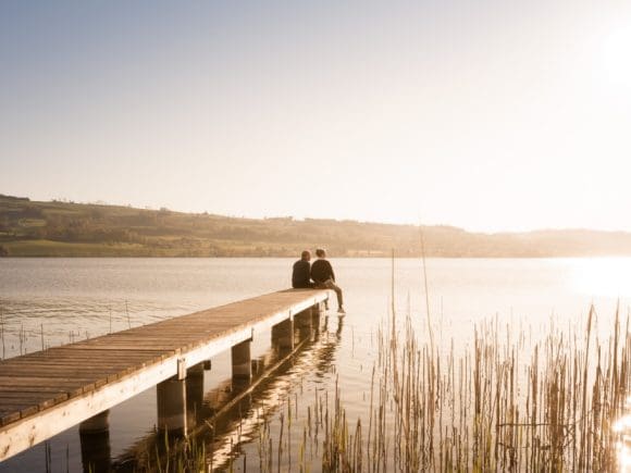 Mann und Frau sitzen auf Pier am See.
