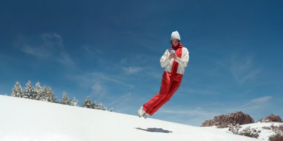 Woman jumping on snow holding a smartphone