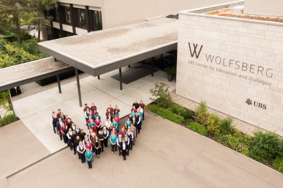 Mitarbeitende vom Wolfsberg stehen als W vor dem Haupteingang des Wolfsbergs