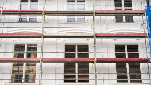 A building is being renovated. This is always a good opportunity to opt for energy-efficient construction or refurbishment. The picture shows an old building whose facade is enclosed in scaffolding.