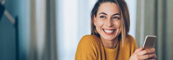 Happy woman sitting with a smartphone over a cup
