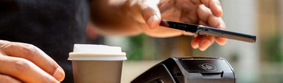 A hand paying for a takeaway coffee with a smartphone via a card terminal