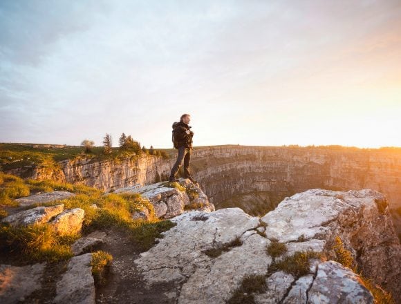 Hiker standing on a mountain cliff in Switzerland at sunrise.