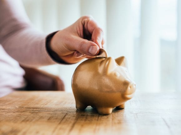 Someone placing a coin into a golden piggy bank