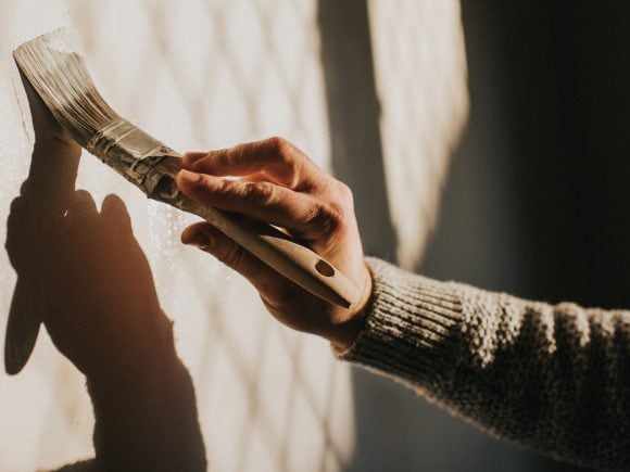 Eine Hand streicht einen Farbpinsel an einer Wand.