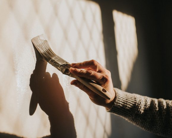 A hand strokes a paint brush on a wall.