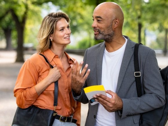 A couple in business attire chat and smile in the park.