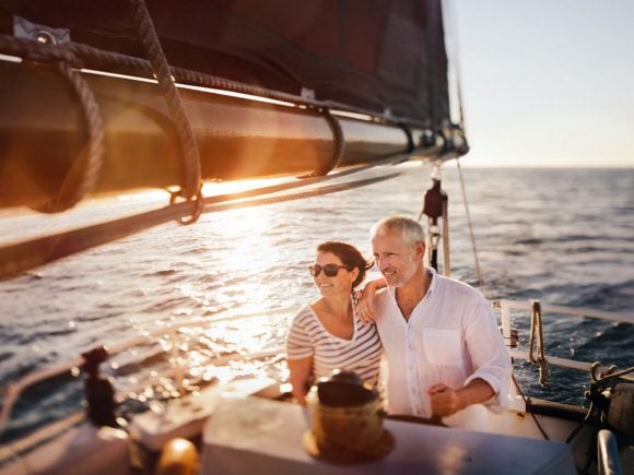 Ein Paar mittleren Alters steht bei Sonnenuntergang auf einer Segelyacht und blickt entspannt über das Meer