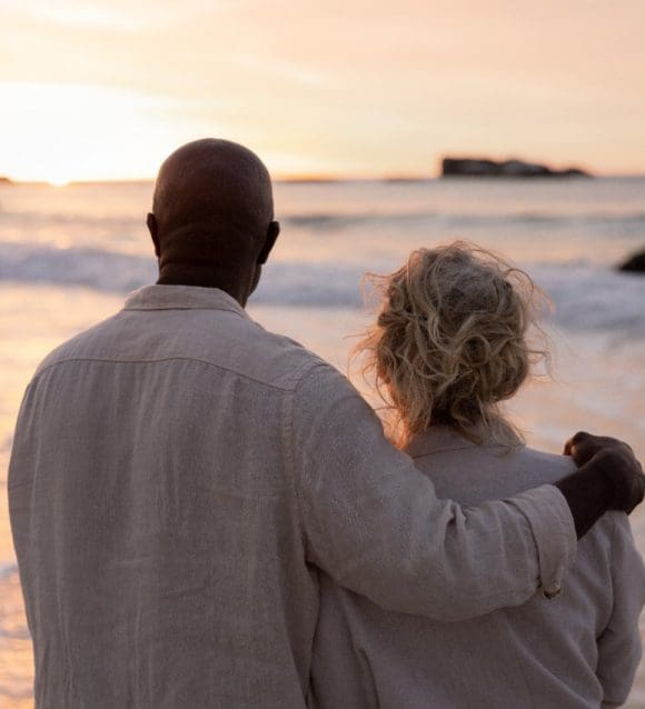 Elderly couple on a beach watching the sunset (view from behind)
