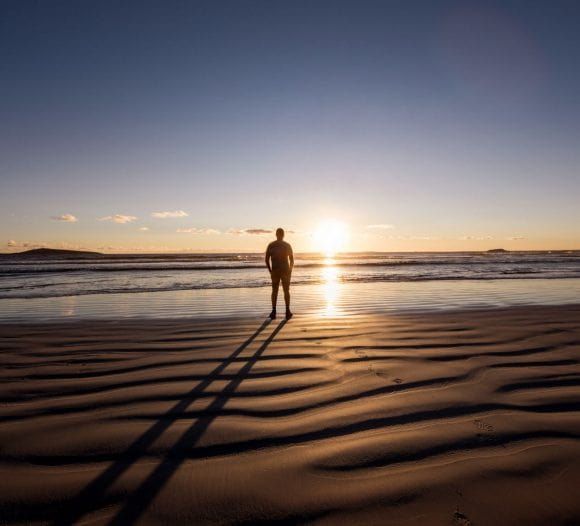 Two men in casual shirts smiling and walking arm in arm on the beach.