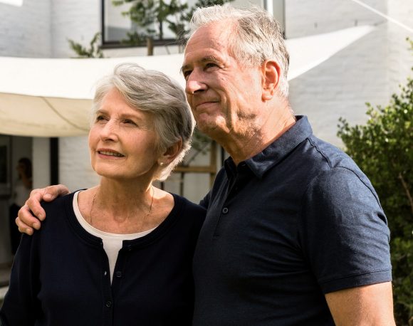 An older and a younger woman are sitting outside on a bench, both wrapped in a blanket.