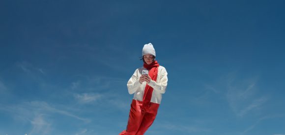 Young man with backpack against the background of skyscrapers happily checking his mobile phone