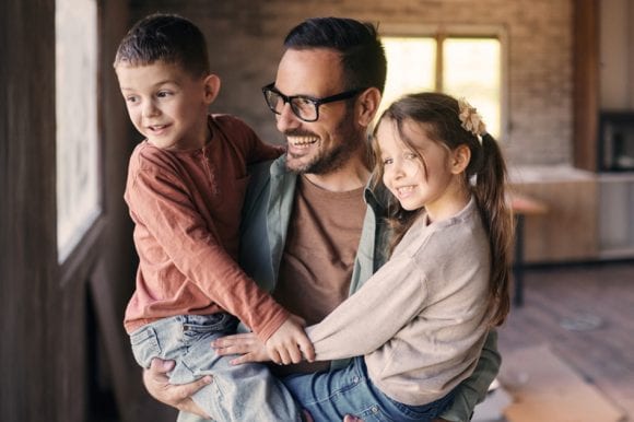 The happy father holding two children in his arm while moving into new home.