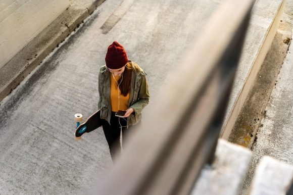 Person mit einer Mütze, die beim Gehen ein Skateboard und ein Smartphone hält