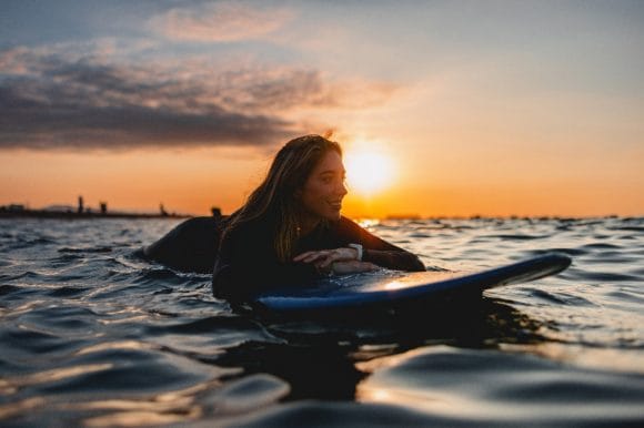 Smiling young woman floating on her stomach on a stand up paddle board at sunset