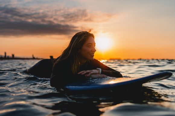 A woman lying on stand-up paddleboard at sunset