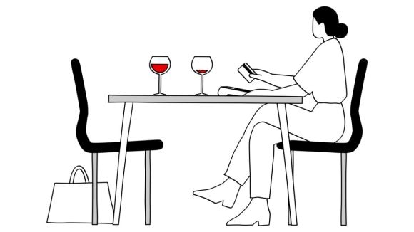 L’illustration montre une table dans un restaurant. Il n’y a plus rien à manger dans l’assiette. À côté se trouve un terminal de paiement avec une carte de crédit argentée posée sur le dessus.