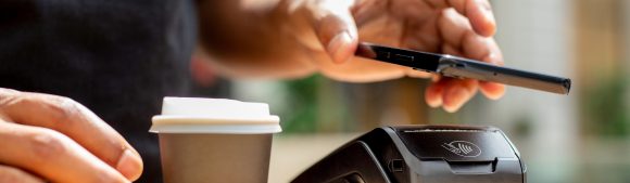 Une main paie un café à emporter avec un smartphone via un terminal de carte
