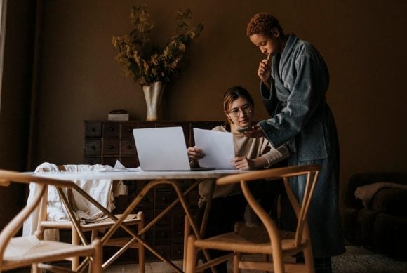 Deux femmes regardant intensément un smartphone et quelques documents près d’une table