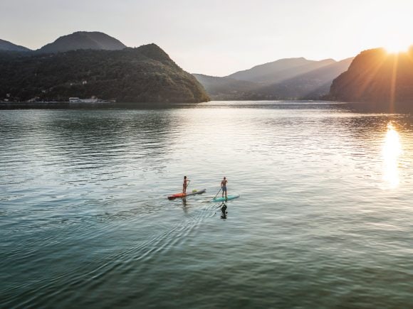 Personne qui fait du stand up paddle sur un lac avec des montagnes en arrière-plan.