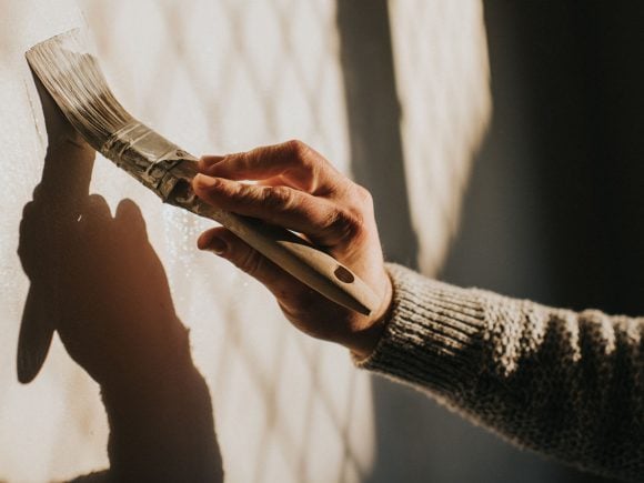 Eine Hand streicht einen Farbpinsel an einer Wand.