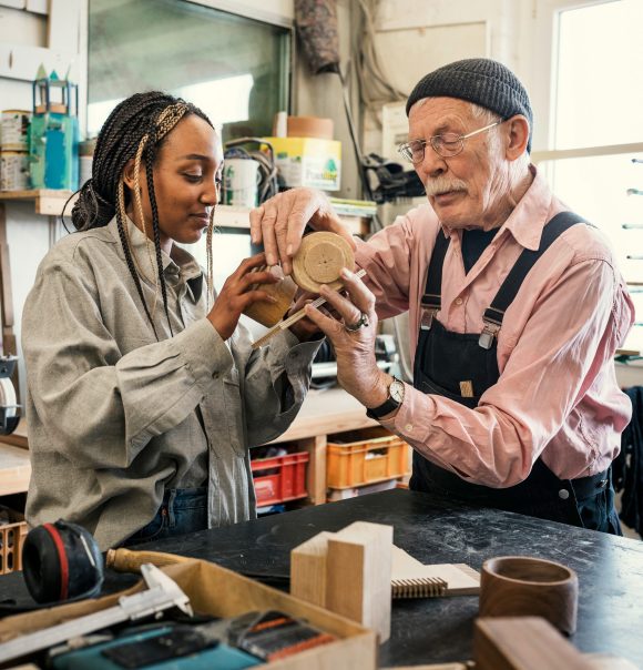 Senior gentleman working with young woman at workbench.