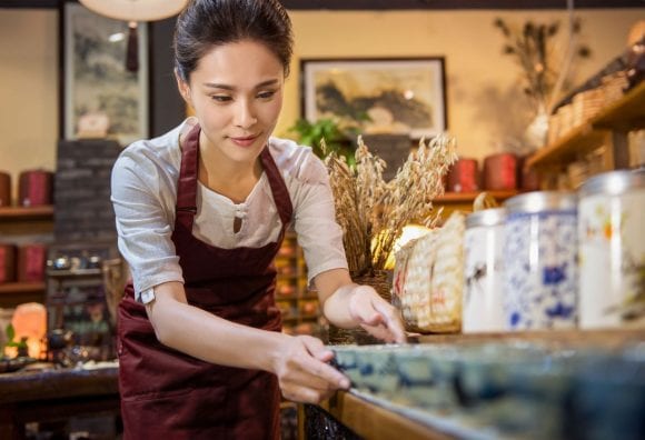 A café employee carefully lines up small tea bowls on the counter.