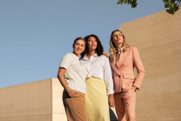 Trois femmes se tiennent avec assurance devant un ciel bleu et des murs en béton beige